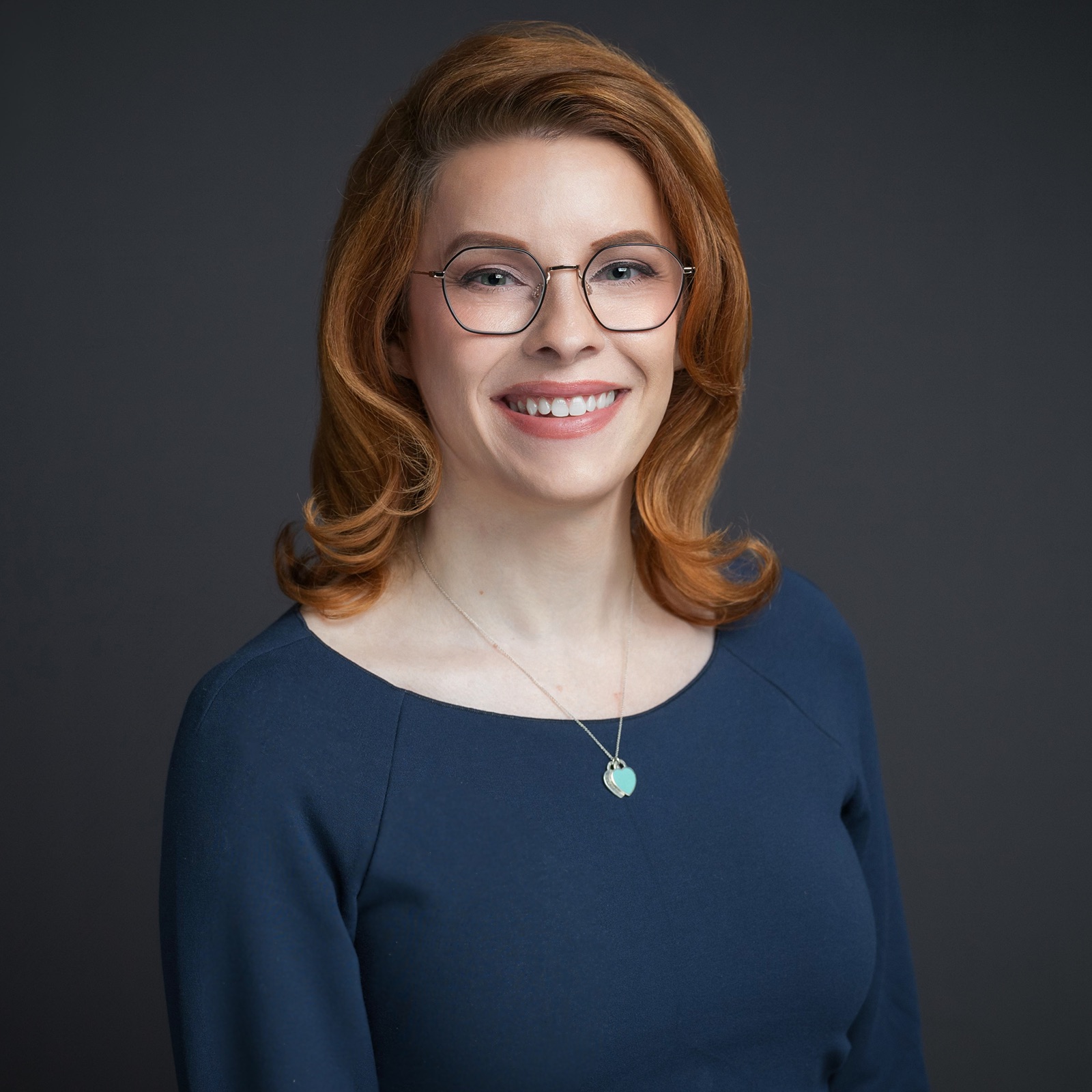 Danni Askini smiling in a navy blouse with Tiffany pendant
